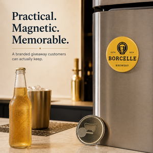 A stainless steel refrigerator or cooler with a circular yellow BORCELLE Brewery magnet on the door and a matching magnet leaning on the bottom edge, shown in a bar-like setting with a glass bottle of amber liquid, a metal cup, and promotional text on a beige wall.