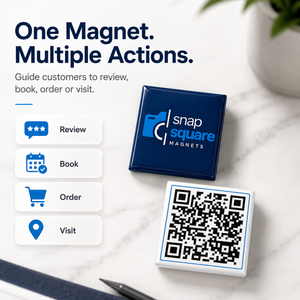 A square snap magnet in dark blue with the 'snap square magnets' logo, shown next to a white square magnet printed with a QR code. The scene is styled on a light marble surface with promotional text reading 'One Magnet.