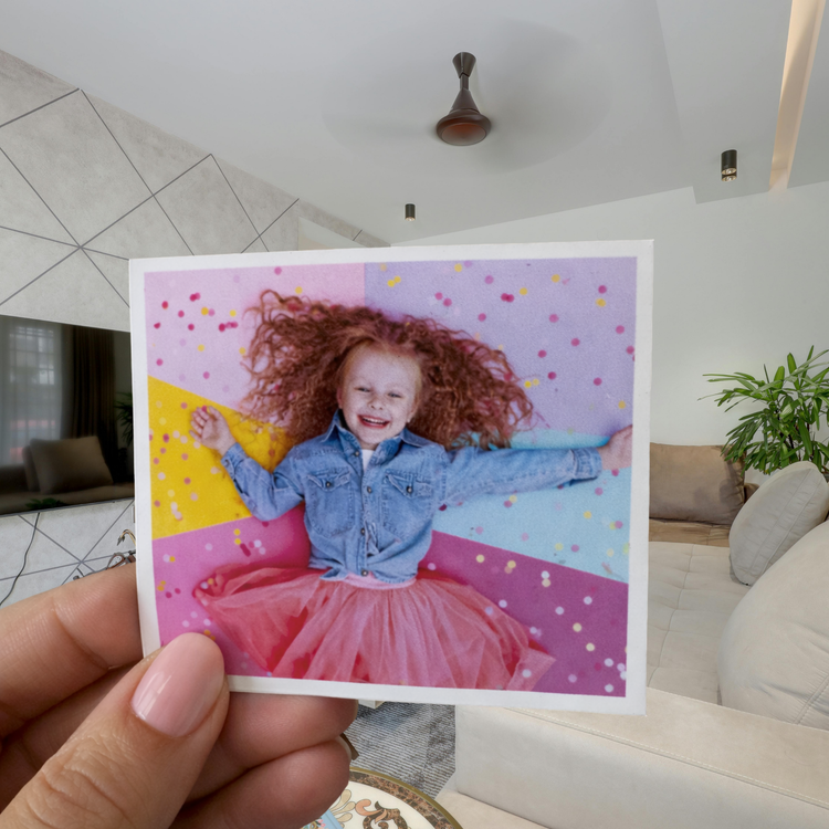 Hand holding a photo of a child with red hair and a blue jacket against a colorful polka dot background.