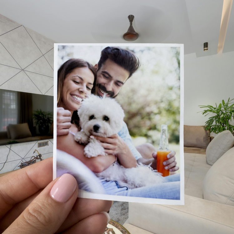 Hand holding a photo of a couple with a dog in a living room.