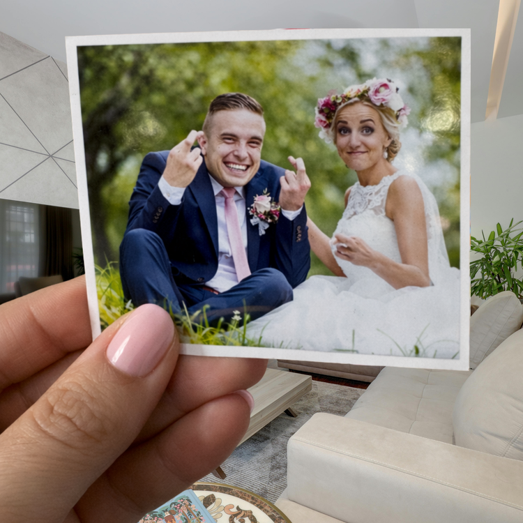 Hand holding a photo of a couple in wedding attire outdoors.